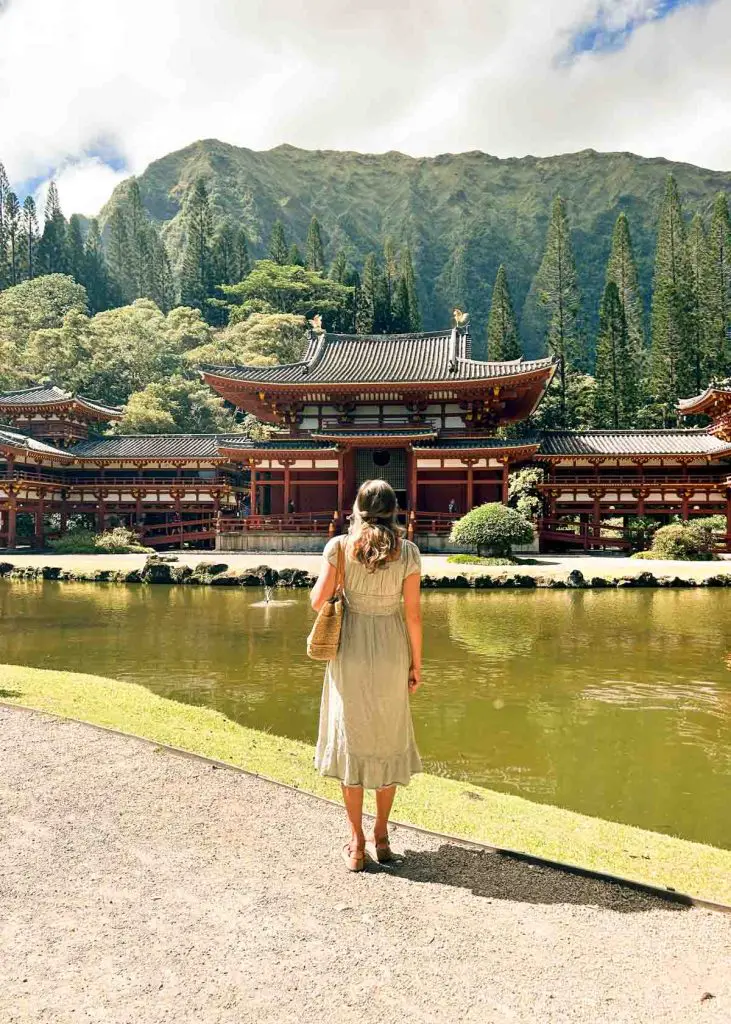 Woman wearing long dress standing in front of the Byodo In Temple in Hawaii with the Ko'olau mountains in the back.