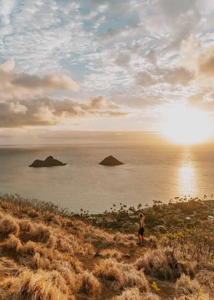 Woman at the top of the Lanikai Pillbox Trail in Kailua, Oahu, with views of the Mokes as the sun rises