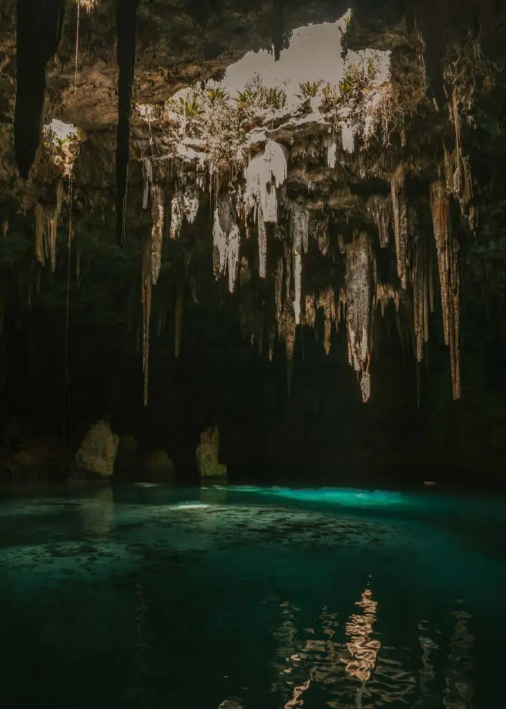 Underground cave cenote with light steaming through into blue water. It is Xcanahaltun Cenote.