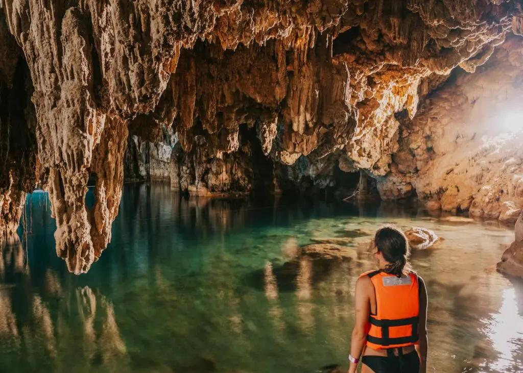 Woman standing in front of stalagmites stalactite next to a small blue pool of water at Dzitnup Cenotes in Valladolid, Mexico