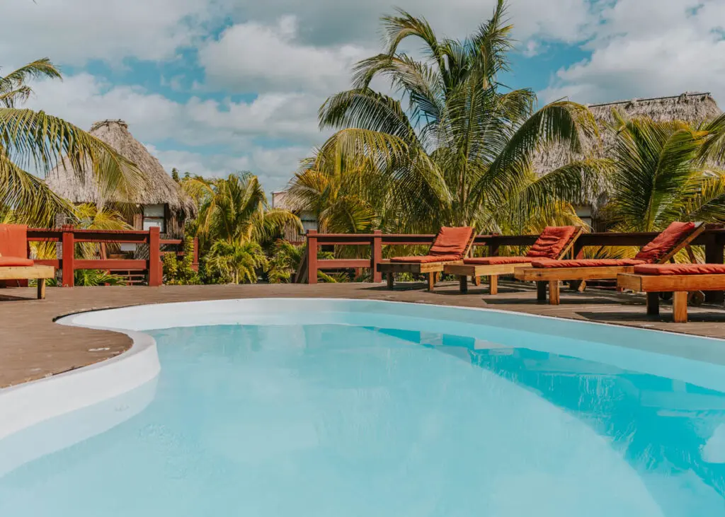 Pool with lounge chairs, palm trees, and cabanas at El Ben on Caye Caulker North Island