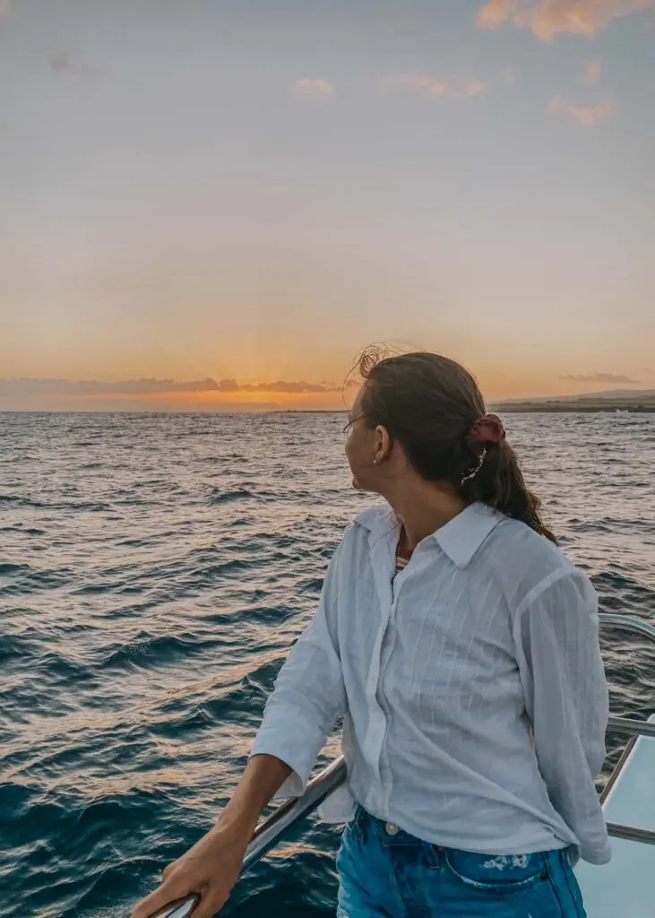 Woman on a catamaran boat looking back as the sunsets over the ocean. This photos of me is from a sunset boat tour on Kauai.