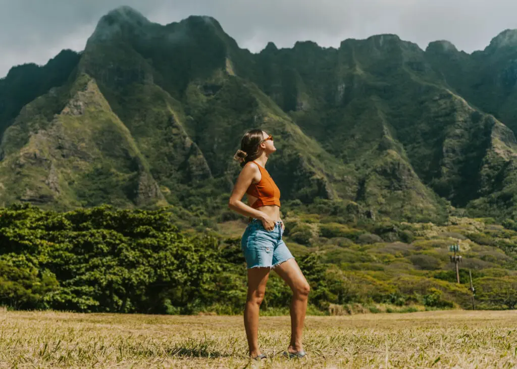 Woman standing beneath vibrant green mountains near Kualoa Ranch, one of the most popular places to visit for your first time on Oahu