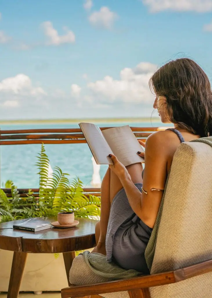 Woman reading on a balcony overlooking Bacalar lagoon at Puerta del Cielo Hotel Origen.