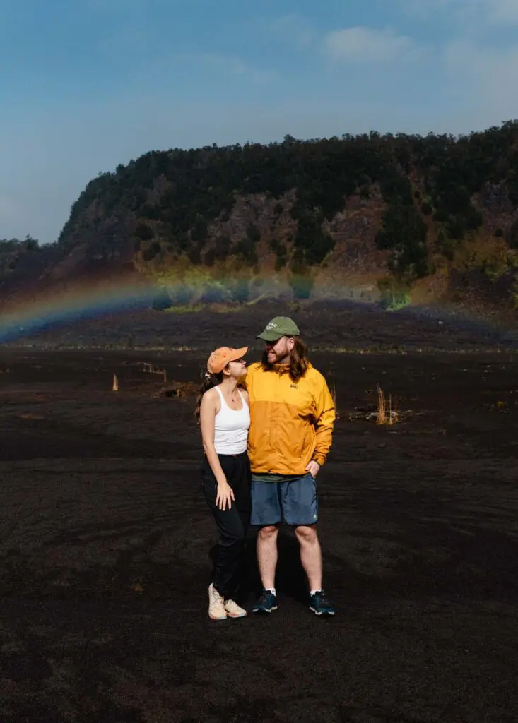 Couple standing on volcanic crater with rainbow in the background on Hawaii's Big Island
