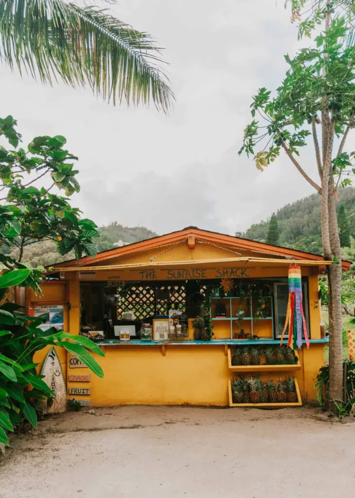 Yellow building between foliage with the name 'The Sunrise Shack', it's one of the most popular places to eat on Oahu's North Shore near Haleiwa