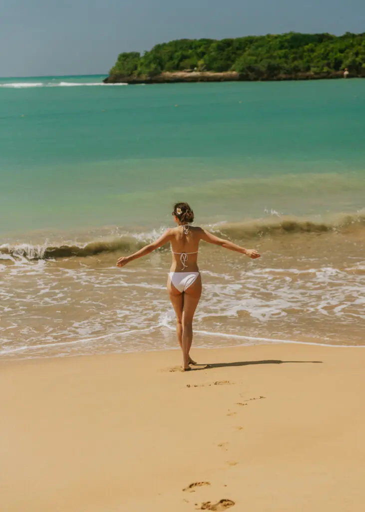 Woman with arms outstretched  walking toward the waves on a golden sand beach in Puerto Rico