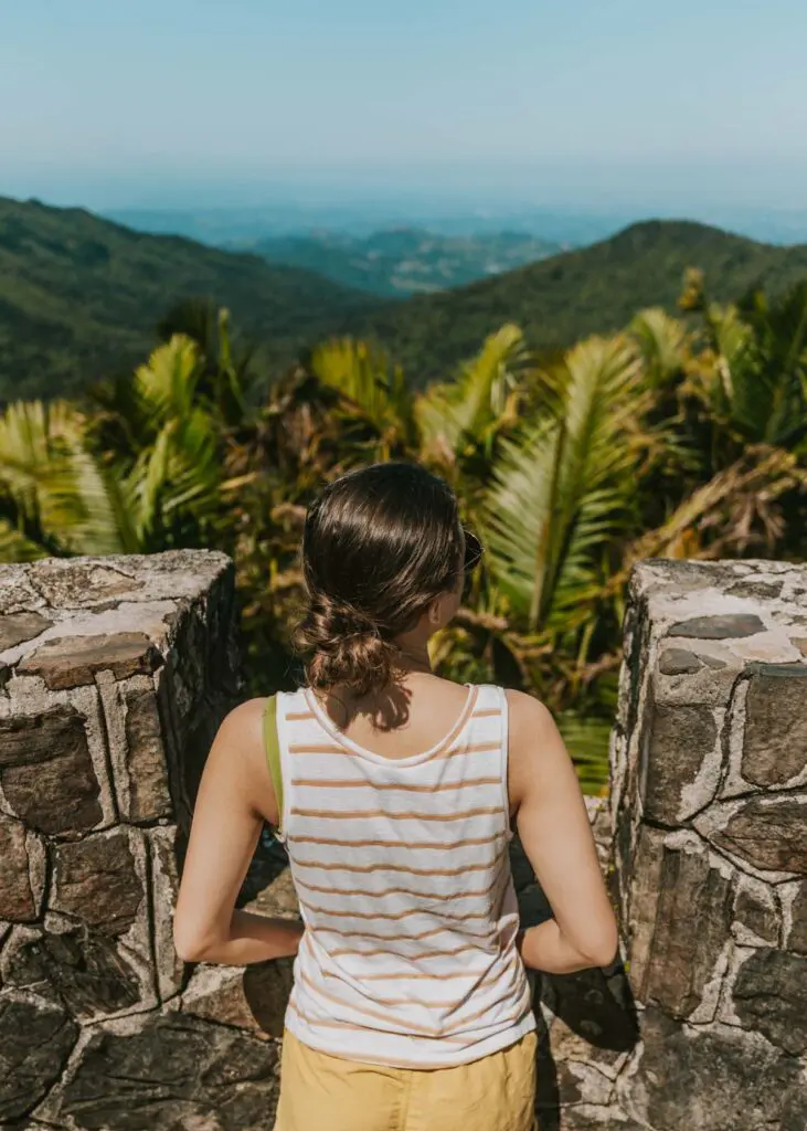 Woman standing at the top of Mt. Britton Tower overlooking the rainforest, mountains, and Caribbean ocean in El Yunque National Forest.