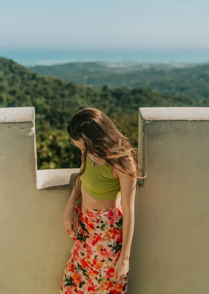 Woman standing at the top of Yokahú Tower in El Yunque with the Caribbean ocean in the background. 