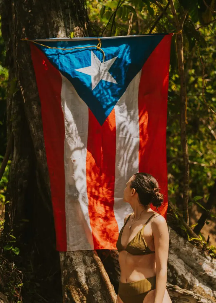 Woman in a green bathing suit looks up at a Puerto Rican flag hanging near the river at Las Pailas near Rio Grande