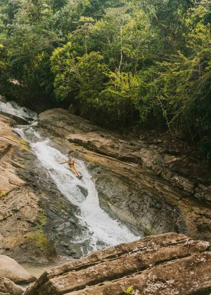 Woman sliding down a waterfall slide near called Las Pailas, which is one of the most fun activities in this Puerto Rico itinerary. 