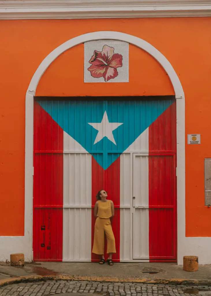 Exploring Old San Juan is a must-do in this 4 day Puerto Rico itinerary! This is a photo of a woman in a yellow set standing in front of a Puerto Rico flag mural in Old San Juan.