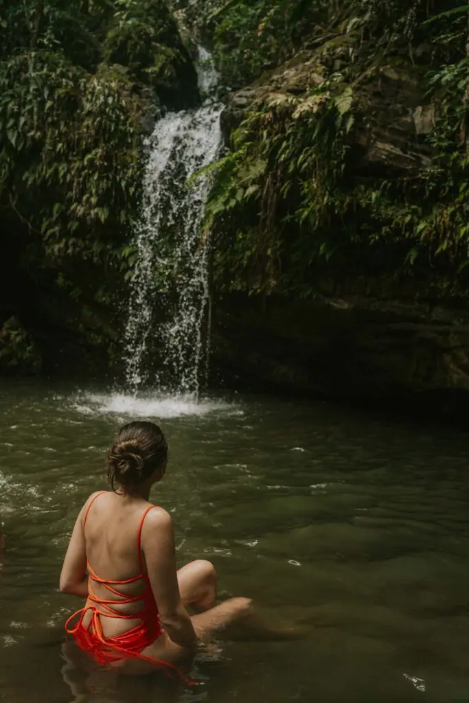 Woman sitting in a shallow pool in front of Juan Diego Waterfall in Puerto Rico.