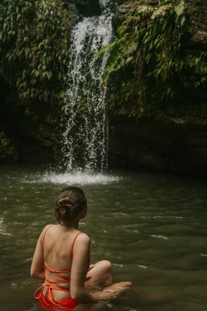 Woman sitting in a shallow pool in front of Juan Diego Waterfall in Rio Grande, Puerto Rico