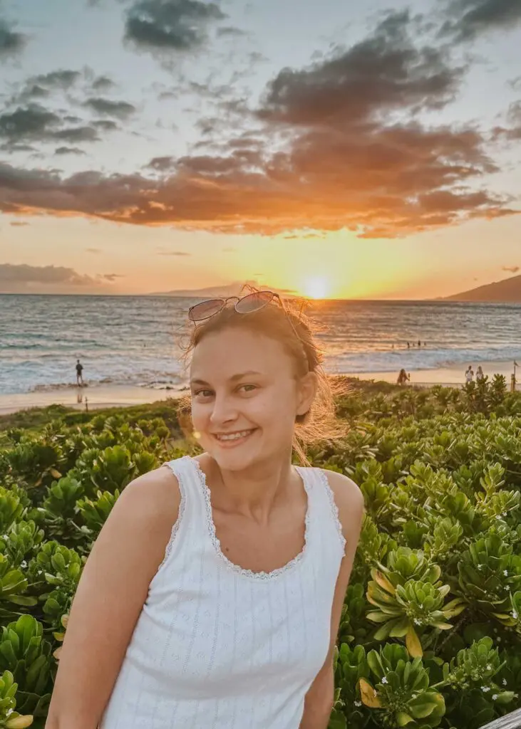 Woman smiles with the sunset behind her at the beach in Kihei, Maui