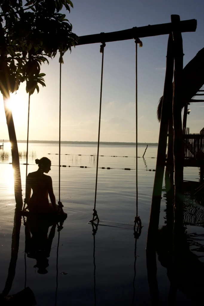 Woman sitting on a submerged swing set in the calm Bacalar lagoon