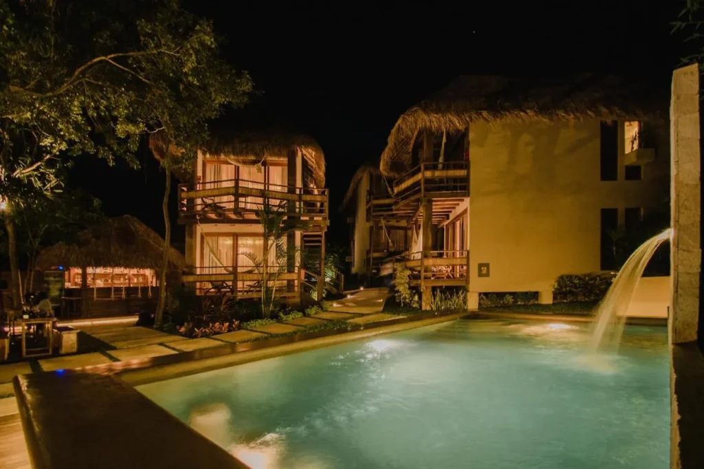 Nighttime shot of Hotel Carolina Bacalar with a small pool and two story thatched roof villas