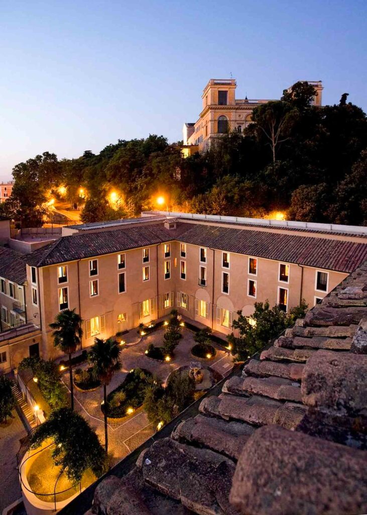 Photo of Donna Camilla Savelli hotel in Trastevere Rome, taken at dusk with glowing lights and Janiculum Hill in the background