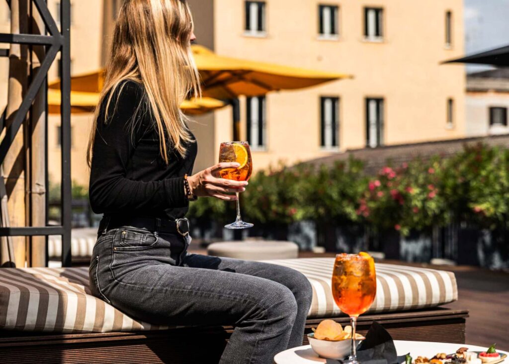 Woman holding an aperol spritz on the patio at Horti 14, a boutique hotel in Trastevere, Rome