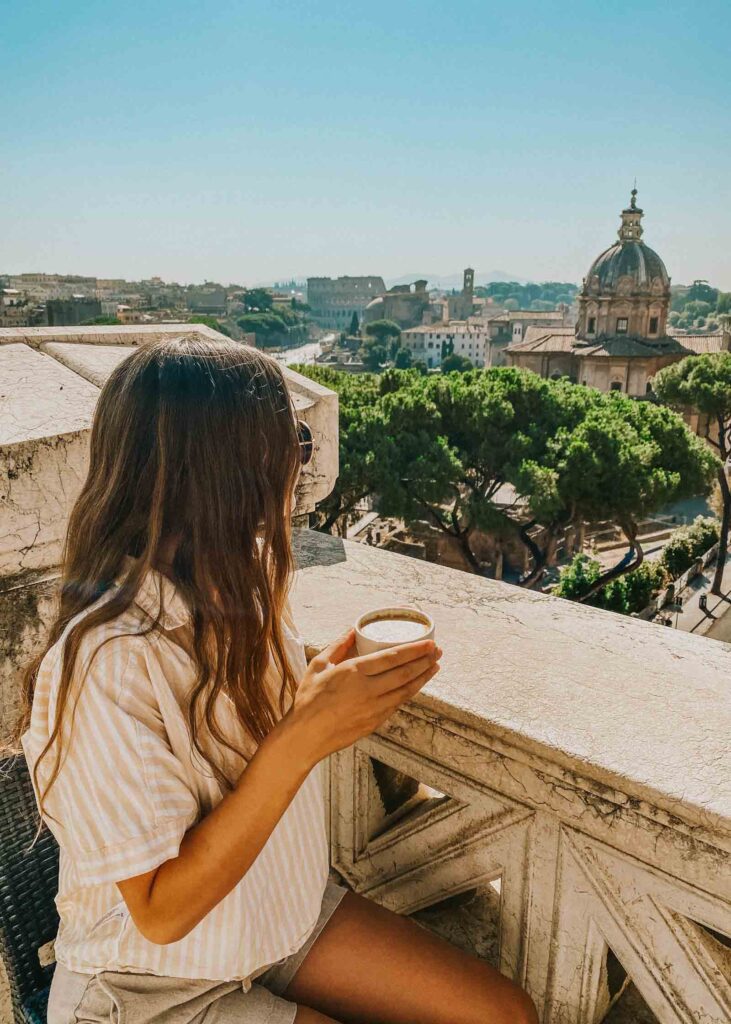 Woman holds a cappuccino while overlooking the Roman Forum, with the Colosseum in the distance 